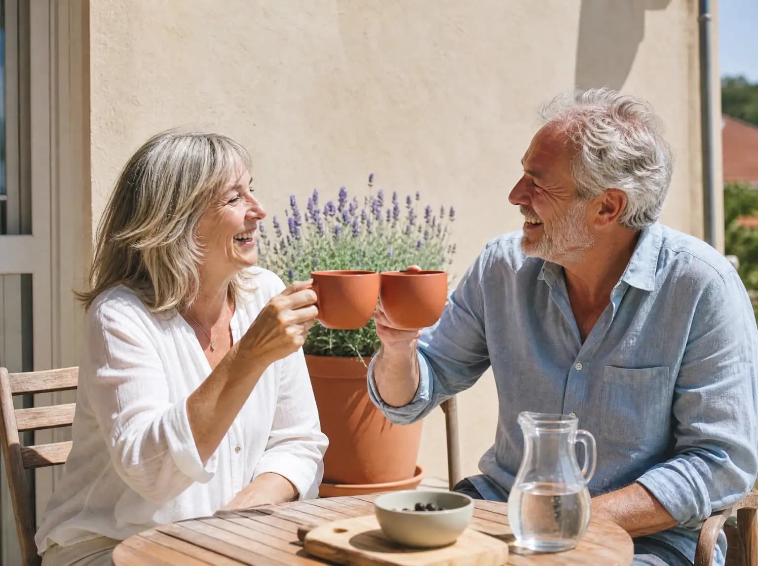 Un couple d'une soixantaine d'années trinque avec deux tasses en terrasse.
