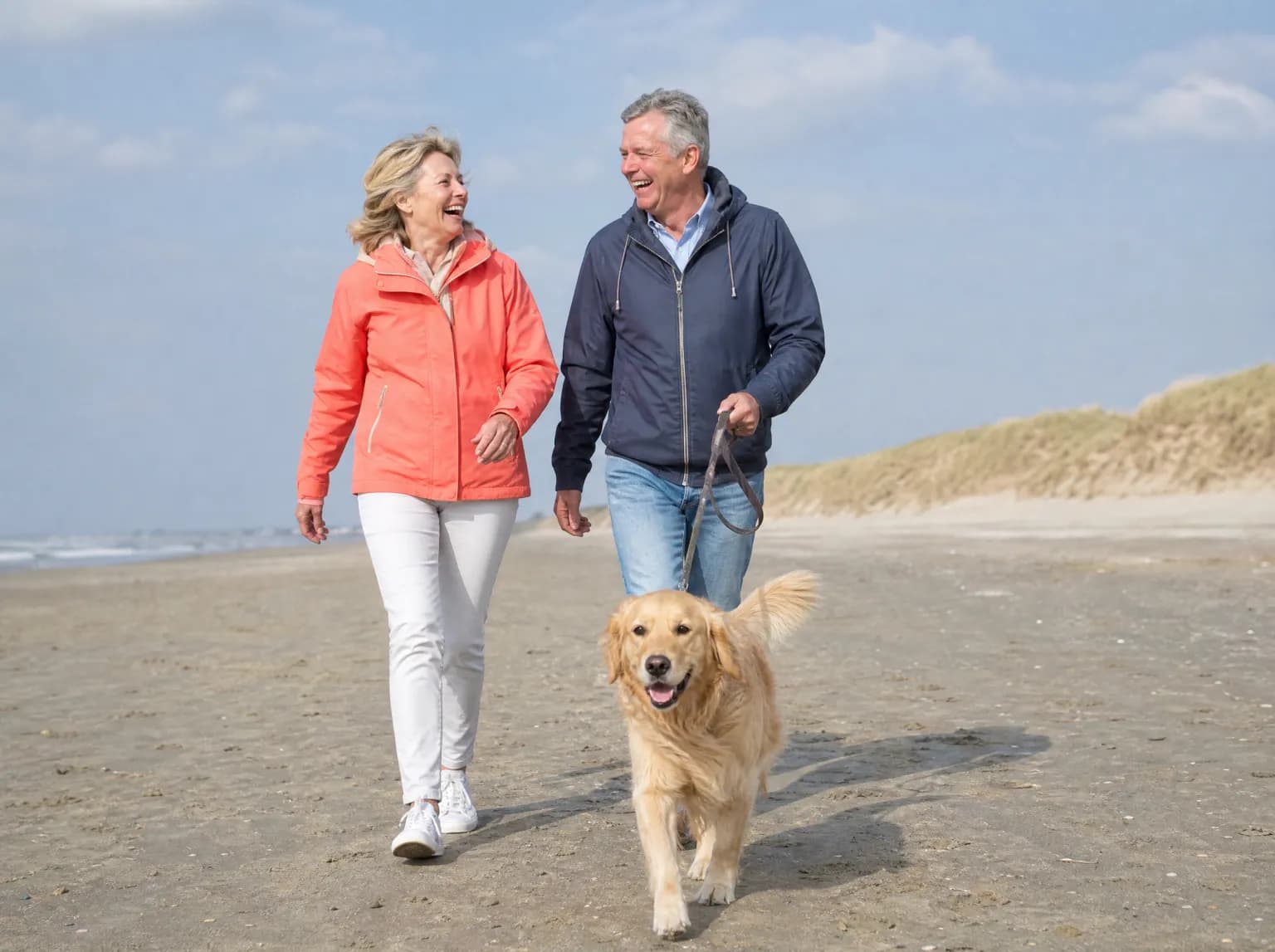 Un couple d'environ soixante-huit ans promène un golden retriever sur une plage de la mer du Nord.