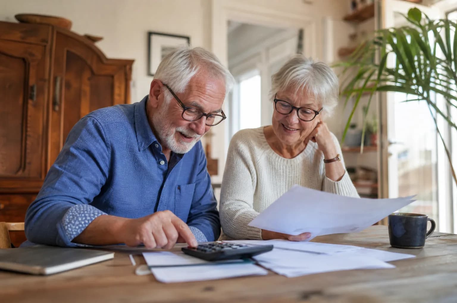 Un couple de retraités examine ses papiers avec une calculatrice à la table du salon