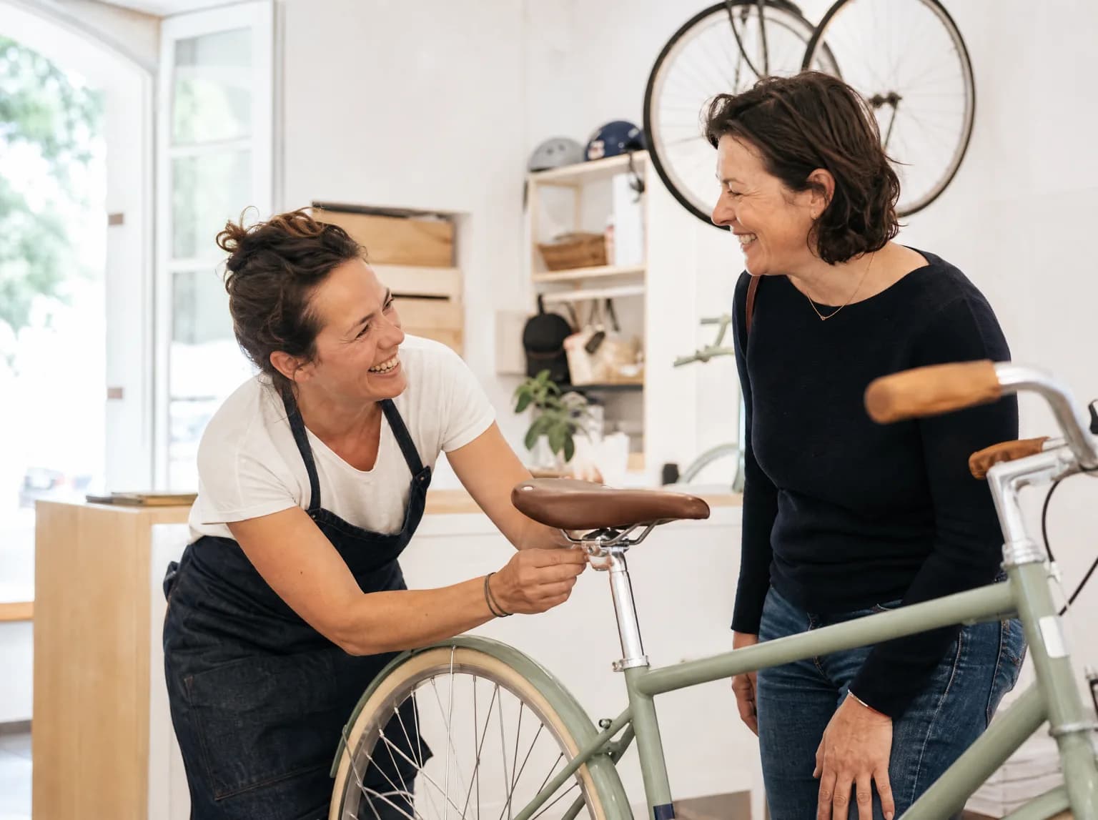 La nouvelle propriétaire d'un magasin de vélos rit avec une cliente en réglant une selle.