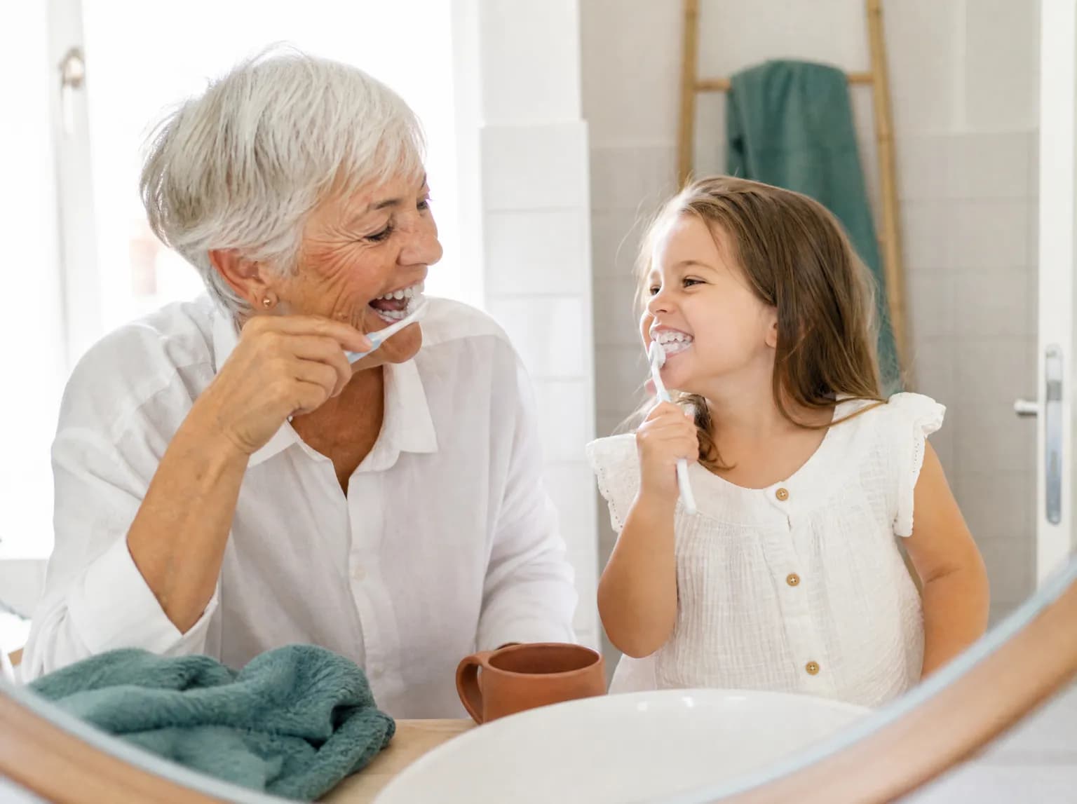 Une grand-mère et sa petite-fille se brossent les dents en riant devant le miroir de la salle de bains.