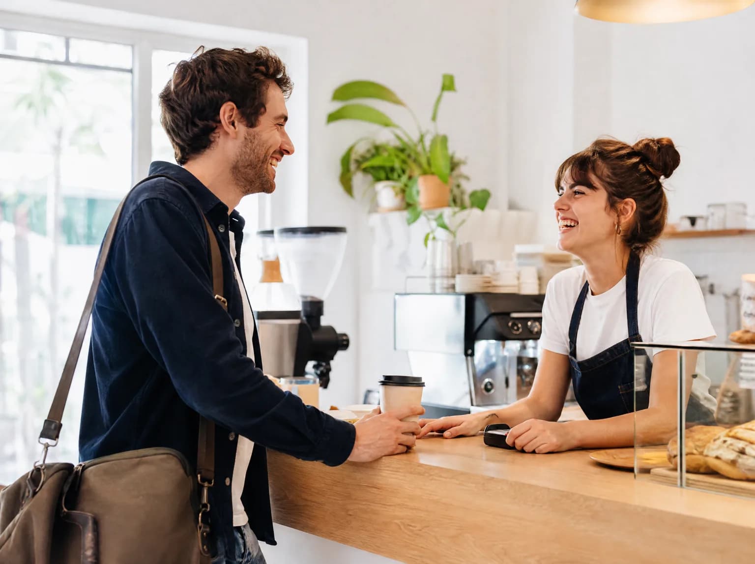 Un jeune indépendant rit avec le barista en récupérant son café au comptoir.