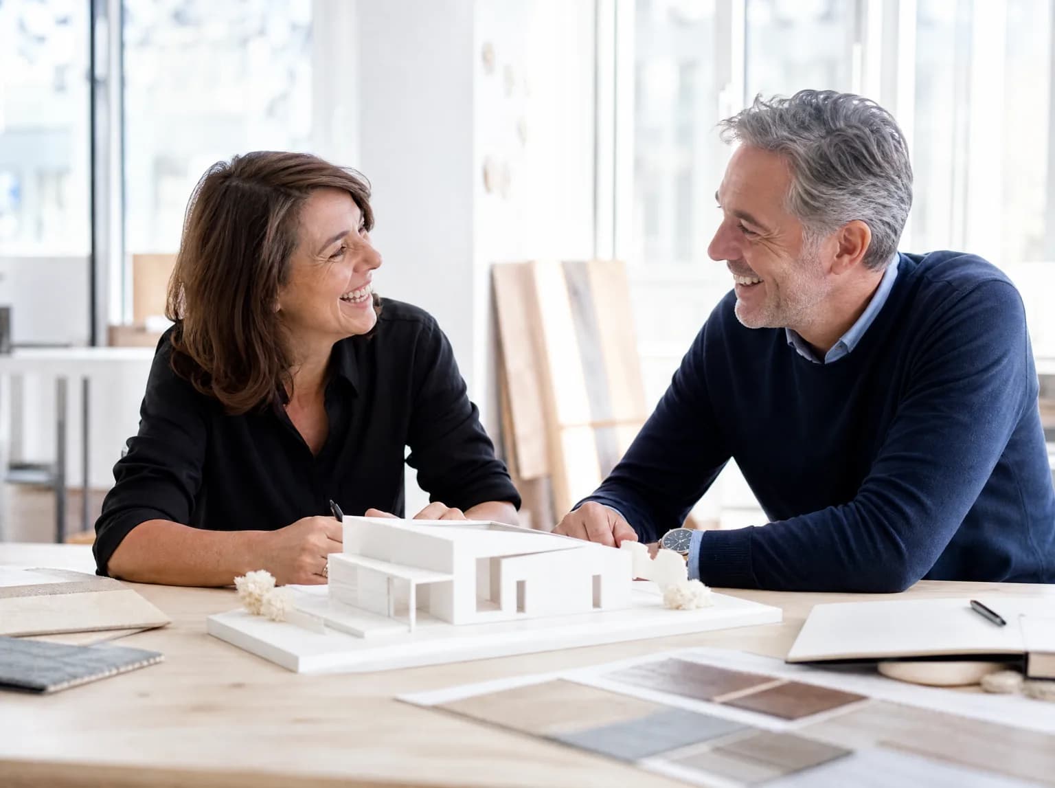 Une architecte d'intérieur rit avec un client devant une maquette blanche.